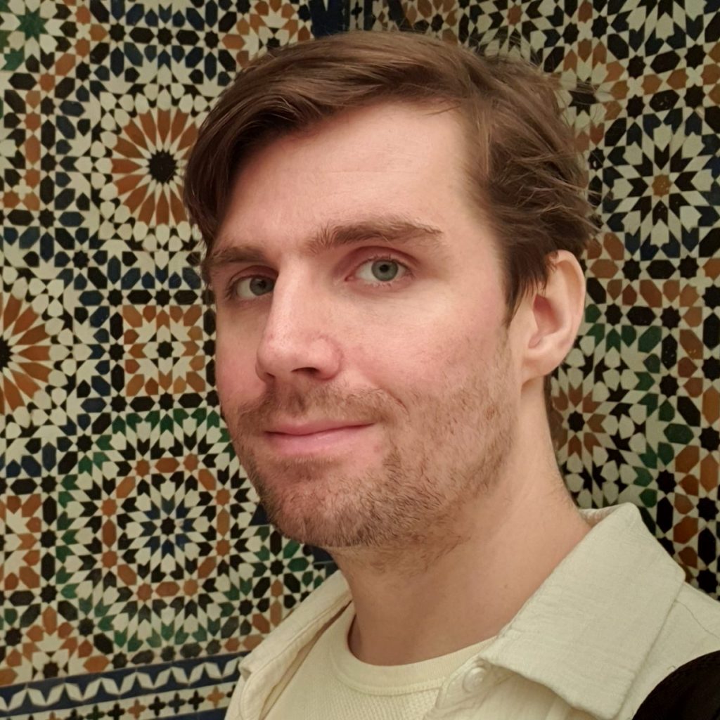 A slightly disappointing man in front of a geometric tile design.