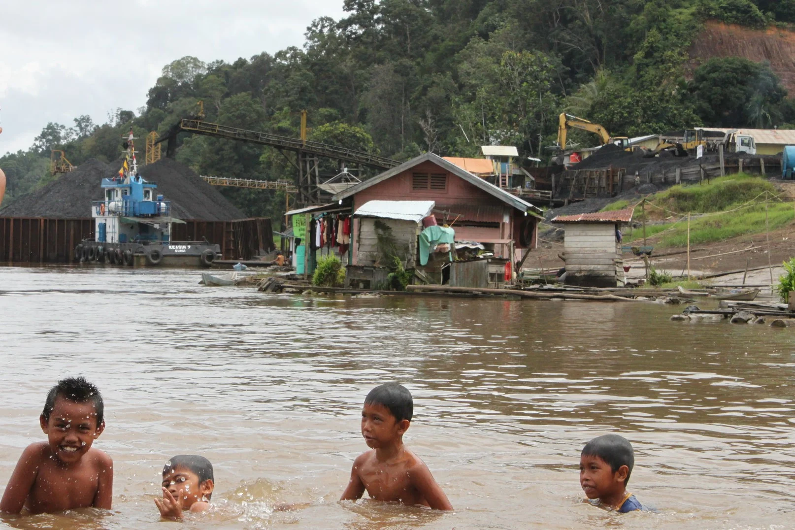 Children playing in a river in Central Kalimantan, Indonesia, as coal barges fill behind them.
