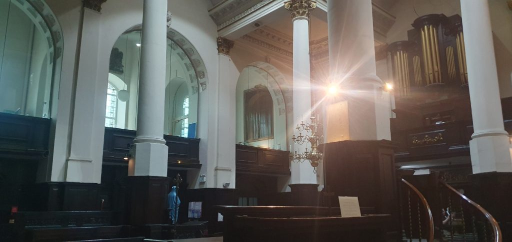 The interior of a church, with great arches to the left of frame and a large organ on an adjacent wall.