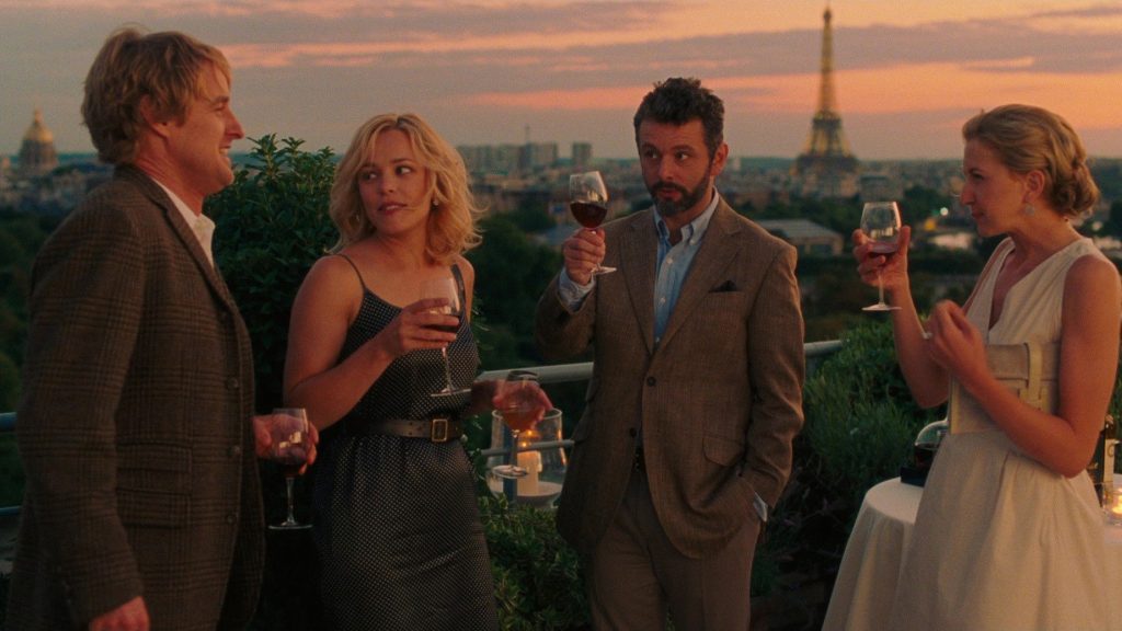 Owen Wilson, Rachel McAdams, Michael Sheen and Nina Arianda's characters drink on a balcony with a view of the Eiffel Tower.