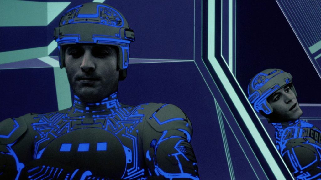 Two grey-faced game-players sit in a digital environment.