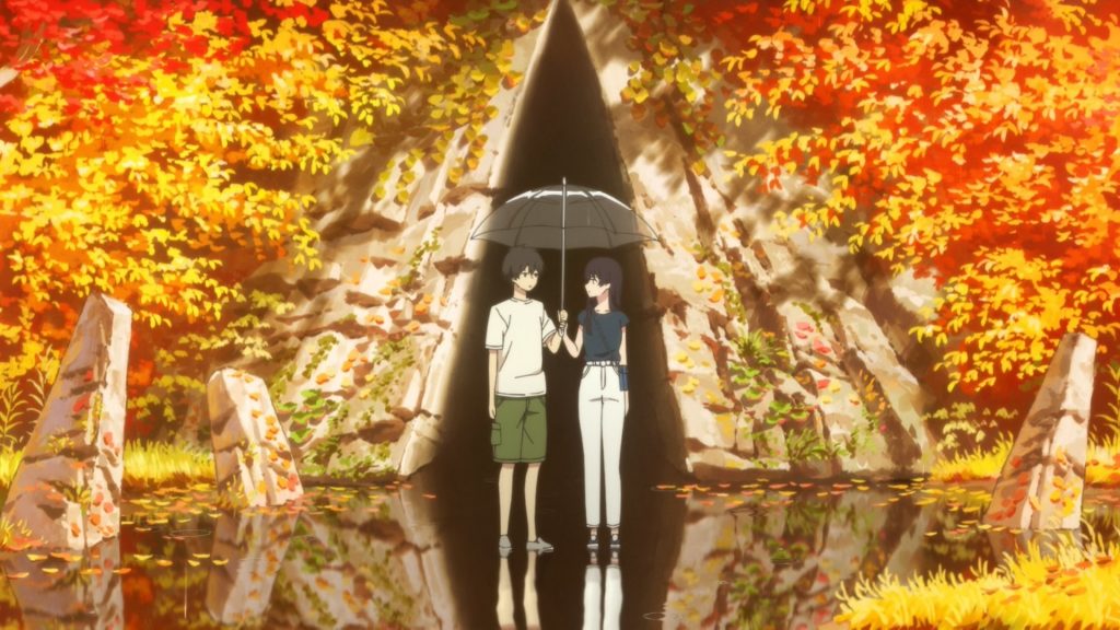 A young couple stand in shallow water, with an ominous cave breaking through the autumn foliage behind them.