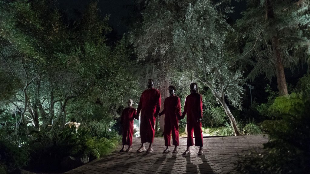 A family in red gowns stand, hand-in-hand, on a driveway in a leafy US suburb.