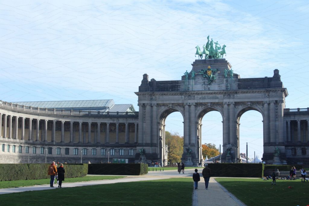 Several groups of people in a park look toward a grand archway