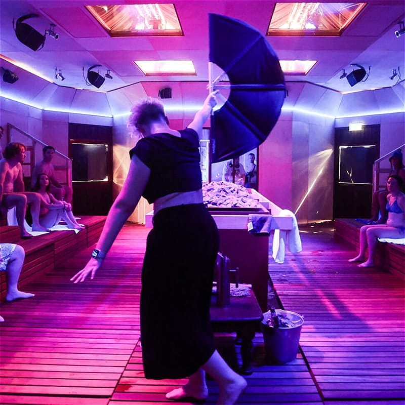 A normally-dressed woman waves a fan in front of sauna attendees.