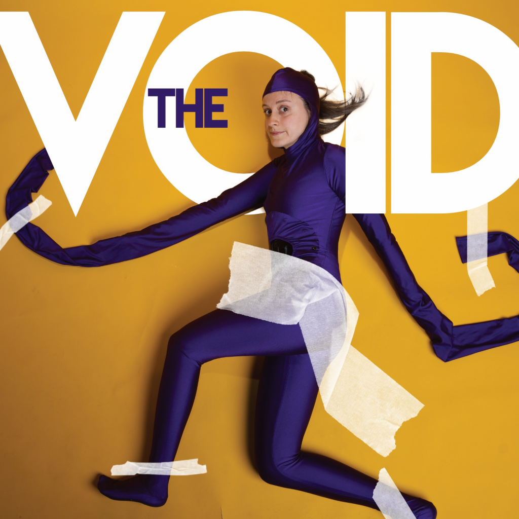 A woman in a purple morph suit with elongated arms is taped to a wall, below the words "The Void".